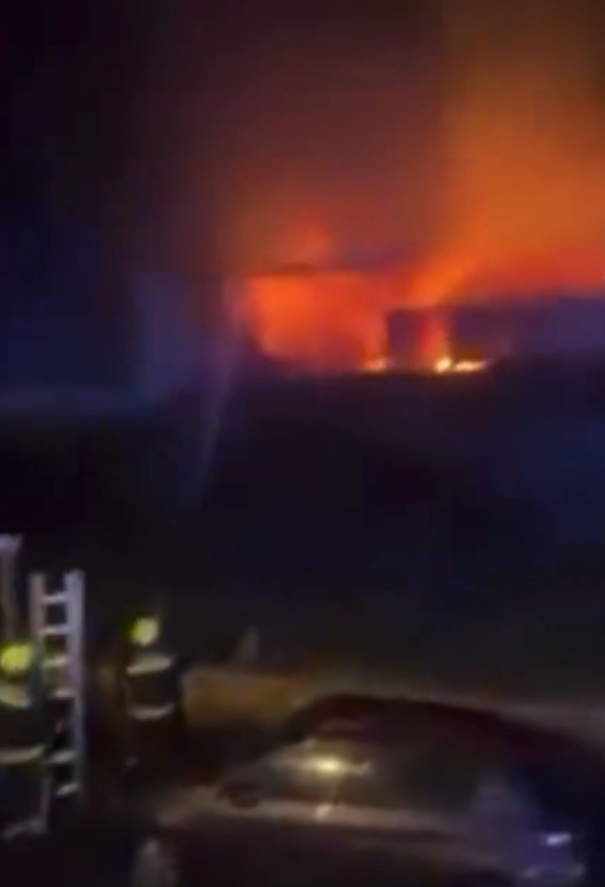 A large building engulfed in flames at night with firefighters present.