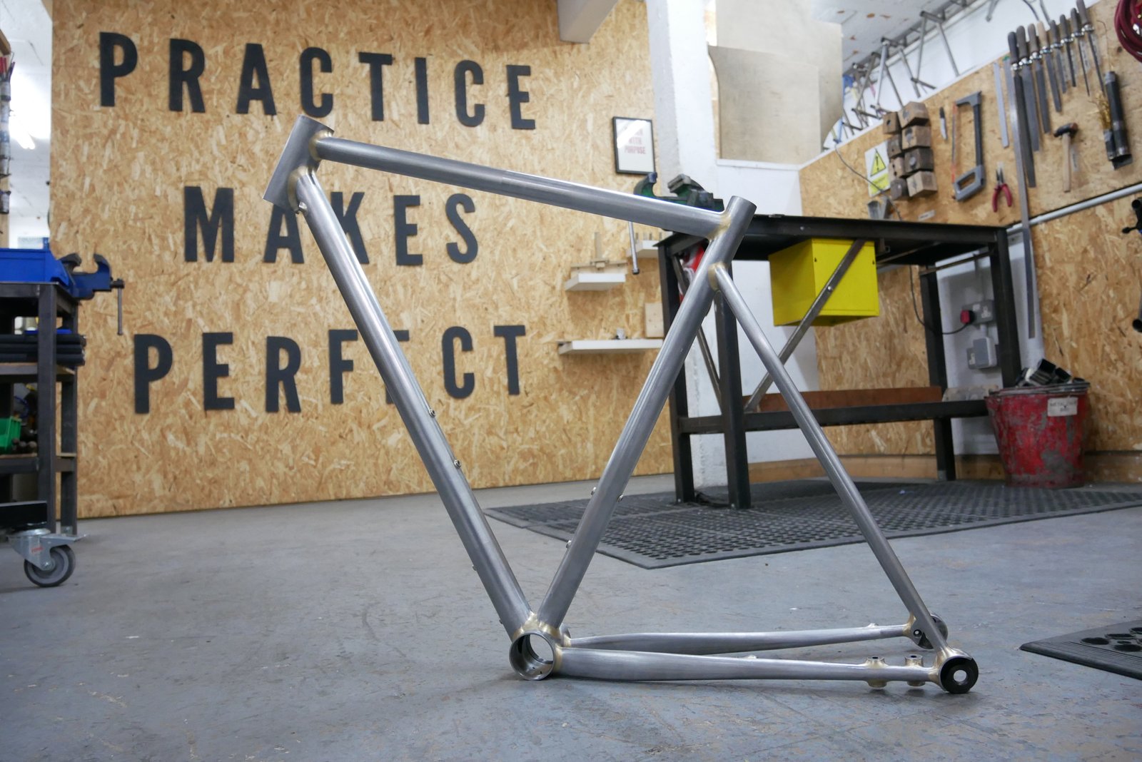 A bike frame sits in front of a sign reading 'Practice makes perfect'
