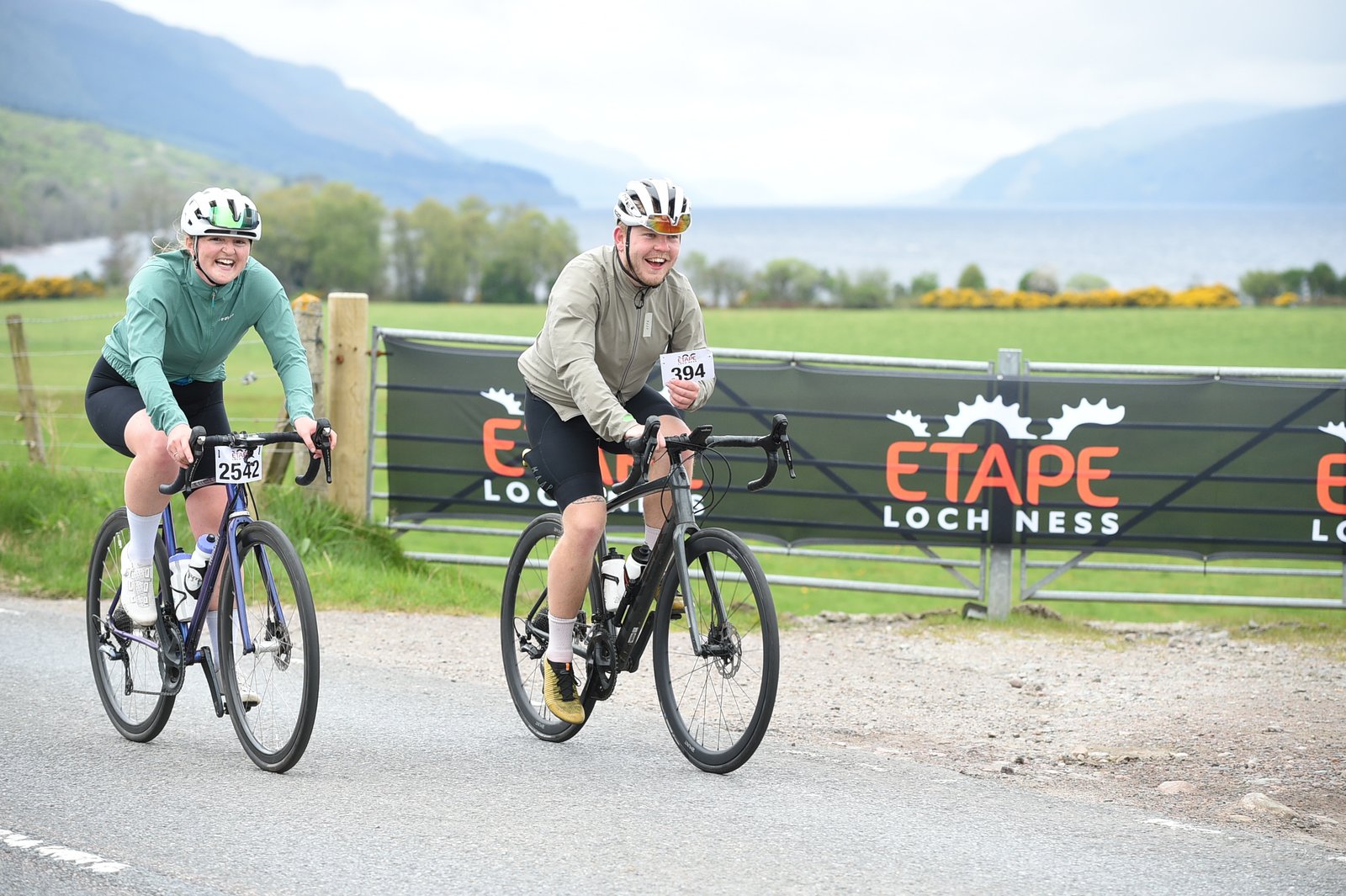 Adam Becket in a beige jacket rides along next to Katherine Moore in a