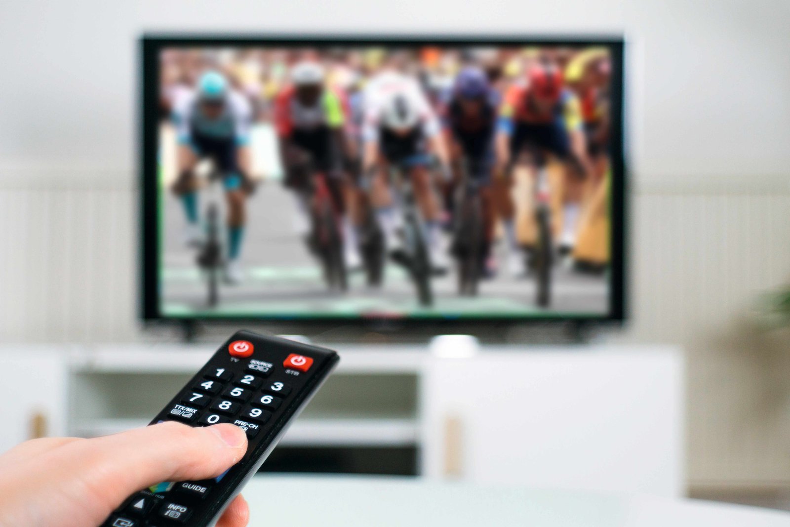A hand holds a remote controller and watches cycling on tv