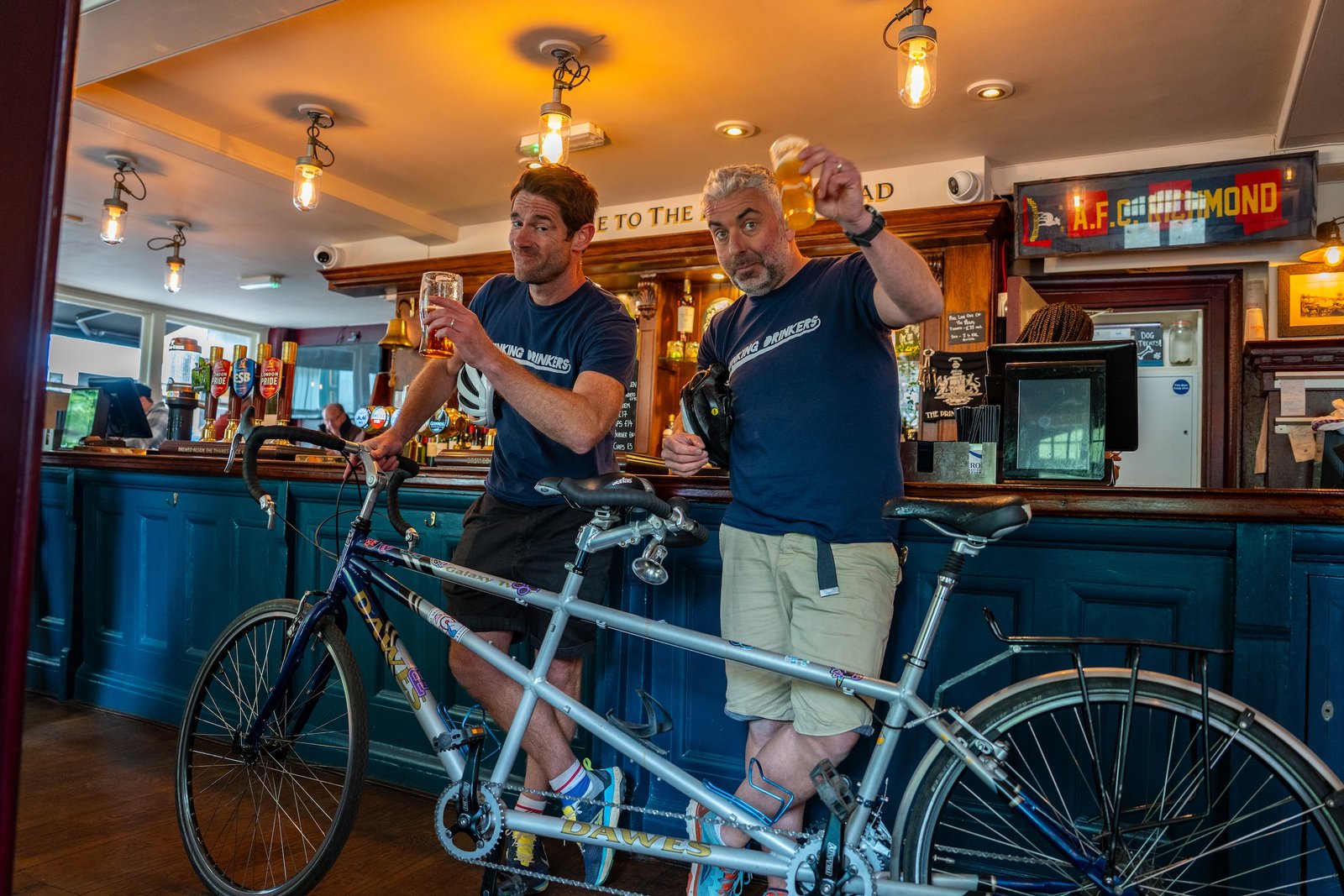 Ben and Tom in a bar with the tandem, raising a glass