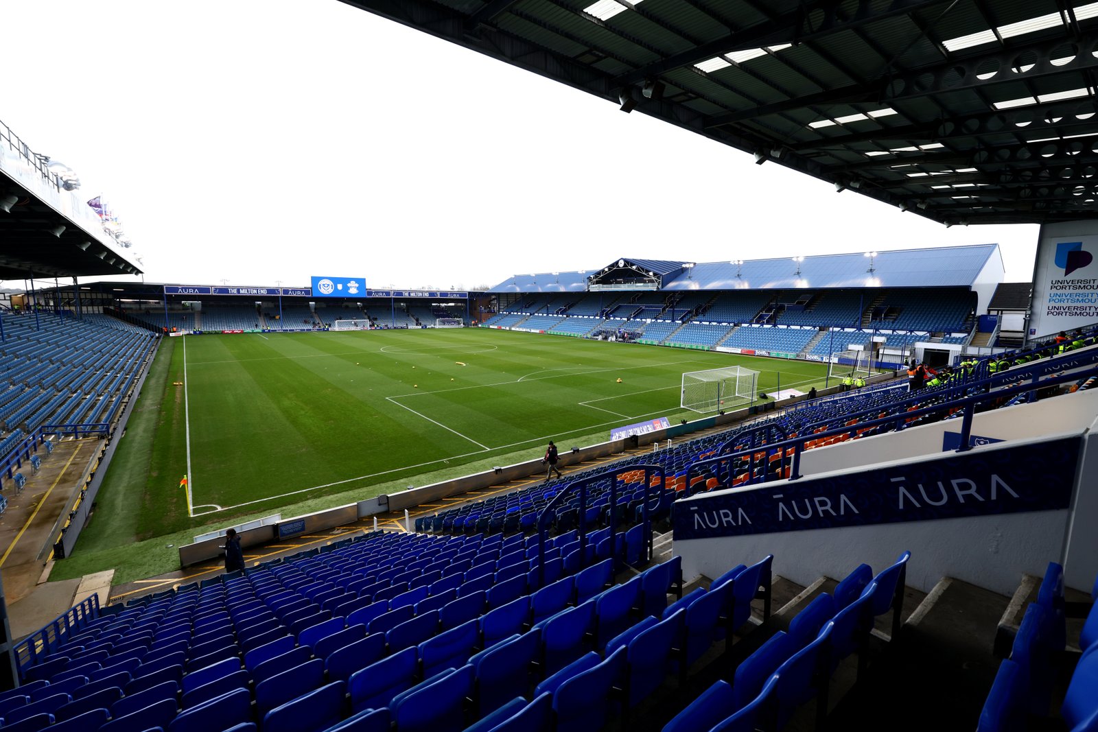 General ground view of Fratton Park with empty blue and orange stadium seats and a green football pitch.