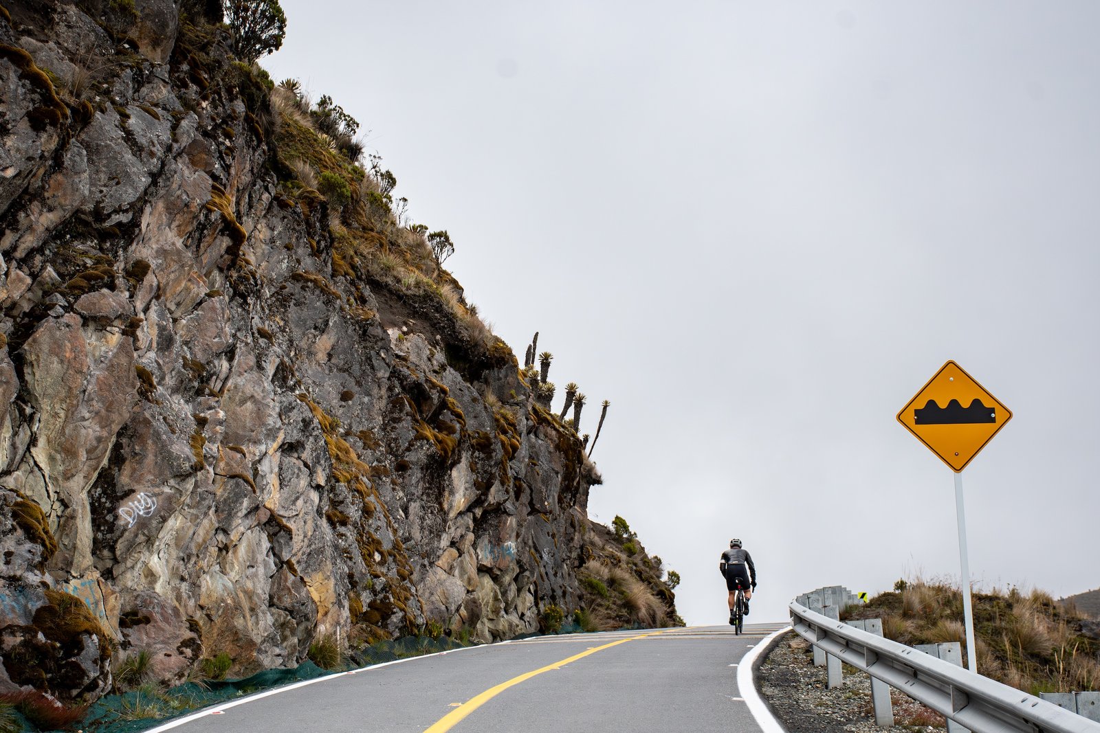 A rider on the horizon, cresting a hill, next to a high gradient yellow warning sign