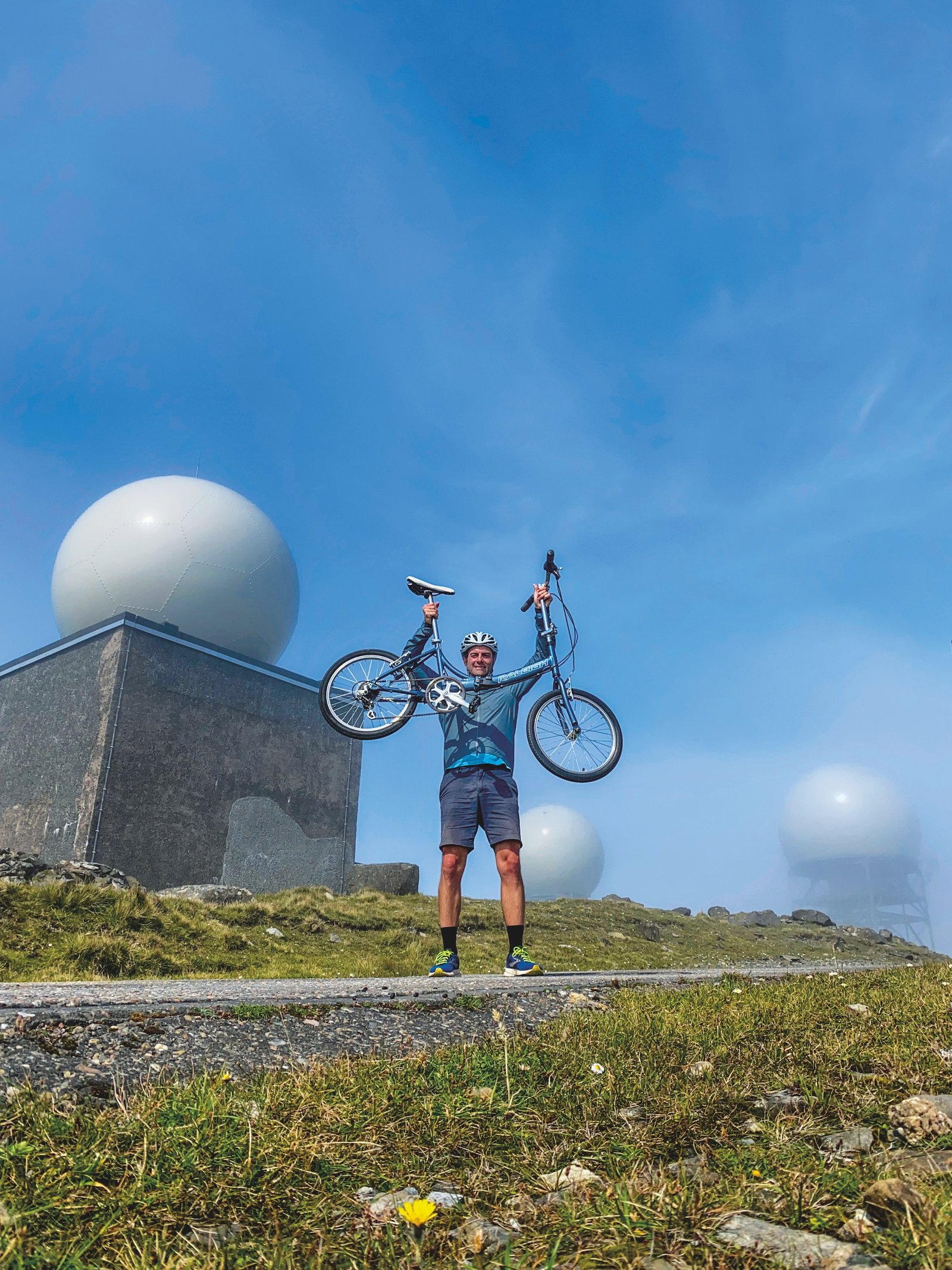 Matt Sparkes holding his folding bike aloft next to the MOD station